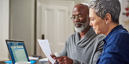Elderly man and woman sitting at a table reviewing financial statements symbolizing retirement planning.
